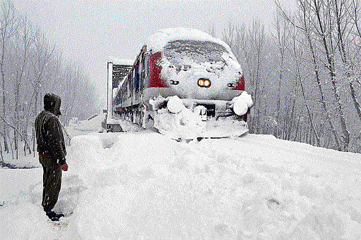 A railway policeman stands guard as a train runs on its tracks amid heavy snowfall in south Kashmir's Anantnag district on Wednesday. PTI