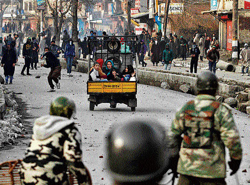 caught in the middle: A three-wheeler carrying a family moves past a protester throwing a stone towards the security  personnel in Srinagar on Friday. REUTERS