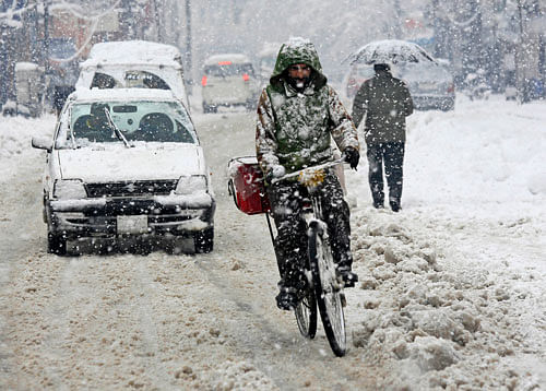 A man cycles on a snow-covered road as fresh snow falls in Srinagar. AP