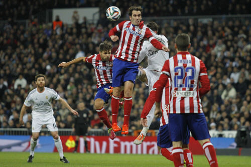 Atletico's Diego Godin, center, jumps for the ball with Real's Sergio Ramos, back, during semifinal first leg of Copa del Rey soccer derby match between Real Madrid and Atletico Madrid at the Santiago Bernabeu Stadium in Madrid, Wednesday Feb. 5, 2014. (AP Photo)