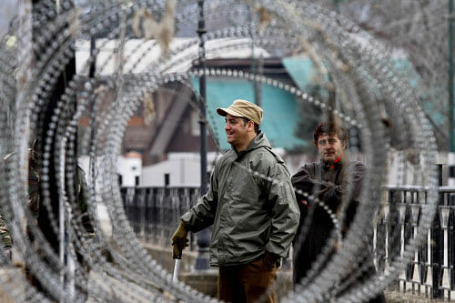 A paramilitary soldier shares a lighter moment with his colleague as a Kashmiri civilian waits to meet his officer for permission to cross the road during a curfew in Srinagar, India, Sunday, Feb. 9, 2014. Thousands of Indian troops fanned out across Indian-controlled Kashmir on Sunday, detaining about 200 separatist activists to prevent protests during a three-day strike to mark the execution anniversaries of two separatists in New Delhi, officials said. AP