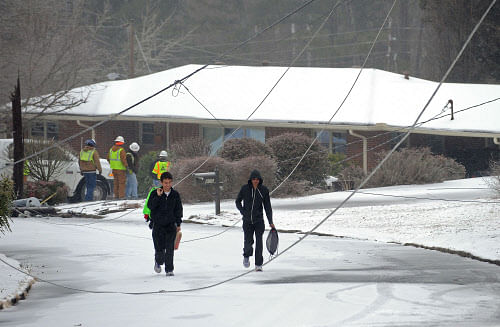Emory University students Hirsh Gaikwad, right, and Tyler Cooke walk through a residential neighborhood past downed power lines after a tree toppled under the weight of freezing rain, sleet and snow and brought down power poles during a winter storm on Wednesday, Feb. 12, 2014, in Atlanta. Over 175,000 residences and businesses statewide were without electricity. (AP Photo/David Tulis)