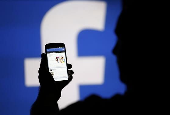 A man is silhouetted against a video screen with an Facebook logo. Reuters.