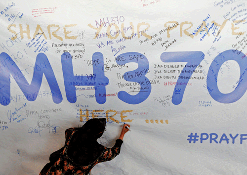 A woman writes a message of support and hope for the passengers of the missing Malaysia Airlines MH370 on a banner at Kuala Lumpur International Airport March 12, 2014. The search for the missing Malaysia Airlines Boeing 777 jetliner expanded on Wednesday to cover an area stretching from China to the Andaman Sea, with authorities no closer to explaining what happened to the plane or the 239 people on board. REUTERS