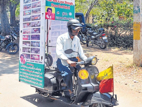 M Khalid rides his scooter with a pole hoarding in the rear of his vehicle, creating awareness against inducement of voters by politicians, in Mysore, on Wednesday. DH Photo