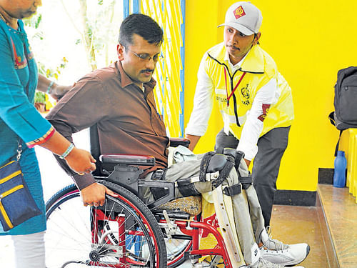 A Civil Defence volunteer helps a physically challenged  person to a voting booth at Banashankari 2nd stage. DH Photo