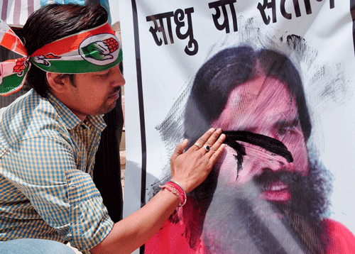 A Congress supporter blackens a poster of Baba Ramdev who made controversial statements on Rahul Gandhi, in Bikaner on Saturday. PTI Photo