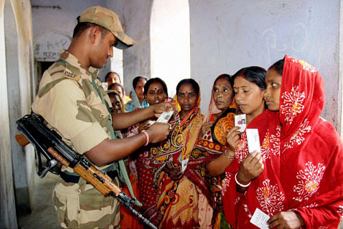 Securityman looks at identity cards of women voters standing in a queue to cast their votes at a polling booth in Burdwan district in West Bengal on Wednesday. PTI Photo