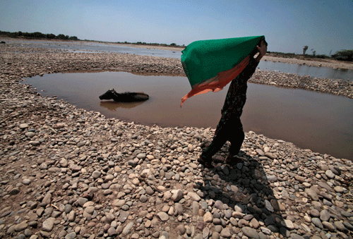 A young girl covers her face to protect from the heat as she walks on a dried bed of the River Tawi on a hot summer day in Jammu, Saturday, May 24, 2014. With the onset of summer, temperature of several places in the north is expected to remain around 43 degrees Celsius. AP