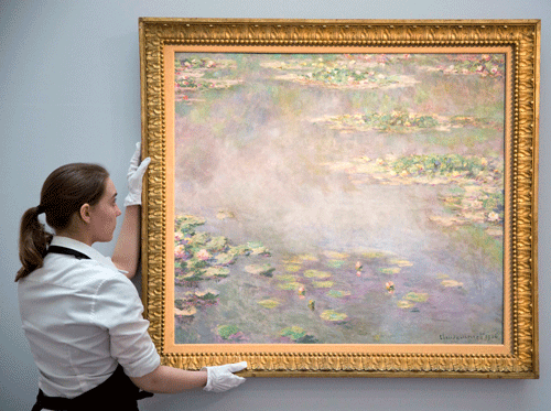 A gallery assistant poses with the painting Nympheas by Claude Monet at a photo-call for Impressionist and Modern Art Evening Sale at Sotheby's auction house in London June 18, 2014. REUTERS