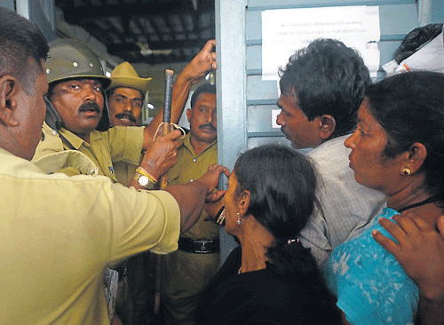 Police personnel prevent people from forcing into the Food and Civil Supplies department office, in Mysore, on Monday. (Right) A flex put up in front of the Department office, explaining the complicated SMS registration procedure. DH PHOTOS