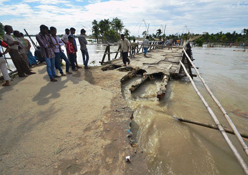 Villagers stand near a damaged bridge on flooded Brahmaputra river at Lawkhowa village in Nagaon district of Assam. PTI photo