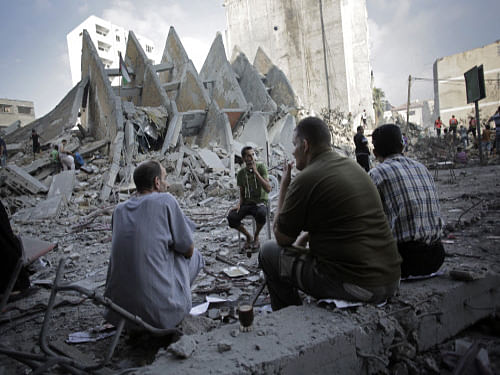 Palestinians have a coffee next to the rubble of the 15-story Basha Tower that collapsed from early morning Israeli airstrikes in Gaza City. Israel and the Palestinians today agreed on a long-term Egyptian-brokered ceasefire to end the devastating 50-day war in the Hamas-ruled Gaza Strip that has killed over 2,200 people. AP photo