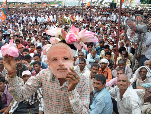 A supporter wearing a mask of Narendra Modi waves BJP symbol 'lotus' at an election rally in Moradabad on Wednesday. PTI Photo