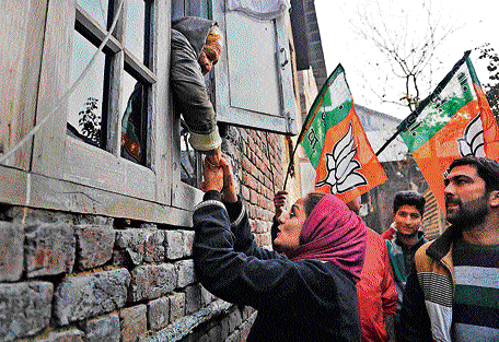 Supporters wave party flags as Bharatiya Janata Party candidate Hina Bhat holds the hand of a Kashmiri woman while campaigning door to door ahead of the assembly elections in Srinagar on Monday. AP