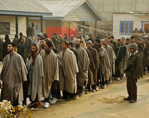 An Indian paramilitary soldier guards as Kashmiri men stand in queues to cast their votes during the third phase polling of the Jammu and Kashmir state elections in Budgham, about 28 kilometers (17 miles) south west of Srinagar. AP photo