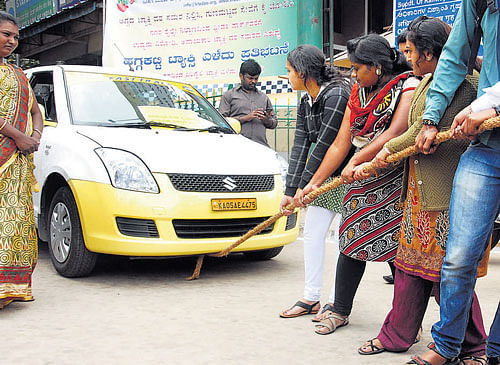 Taxi operators stage a protest against fare war by pulling a cab by rope in the City on Thursday. DH PHOTO