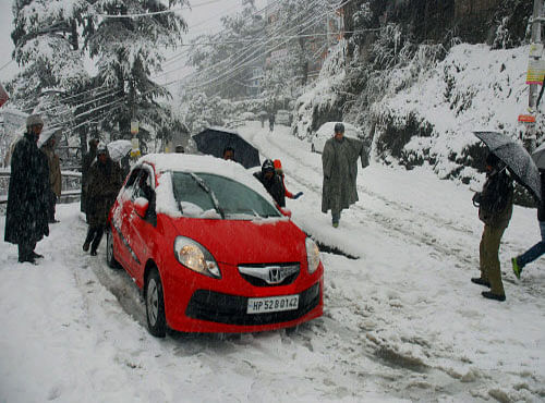 People push a vehicles through a snow covered street after the season's first snowfall in Shimla on Sunday. PTI Photo