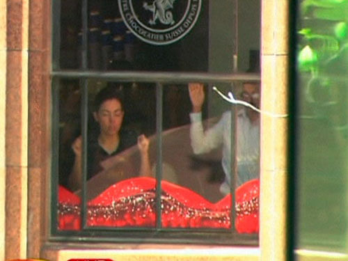 This image taken from video shows people holding up hands inside a cafe in Sydney, Australia Monday, Dec. 15, 2014. A gunman took an unknown number of people hostage inside the downtown Sydney chocolate shop and cafe at the height of Monday morning rush hour, with two people inside the cafe seen holding up a flag believed to contain an Islamic declaration of faith. AP Photo