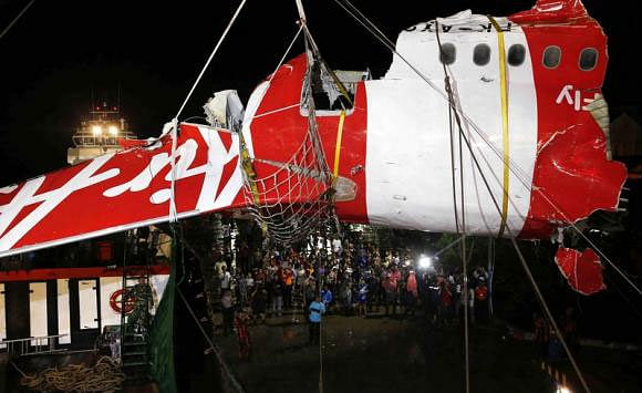 People watch as a section of the tail of AirAsia QZ8501 passenger plane is lifted off a ship and onto the back of a truck, the day after it was lifted from the seabed, in Kumai Port,
