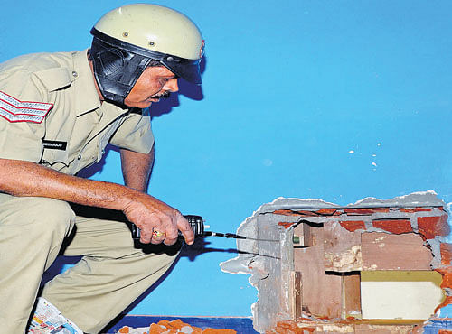 A policeman inspects the hole drilled by burglars into the wall of a jewellery shop at Muneshwara Block, Girinagar, on Monday. DH PHOTO