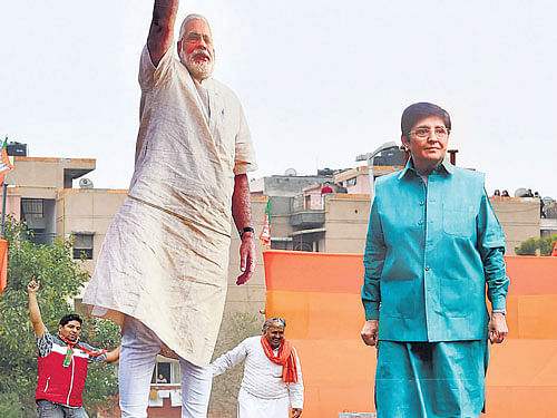 Supporters look on at the cut outs of Prime Minister Narendra Modi and BJP chief ministerial candidate Kiran Bedi during an election rally at Dwarka in New Delhi on Sunday. PTI