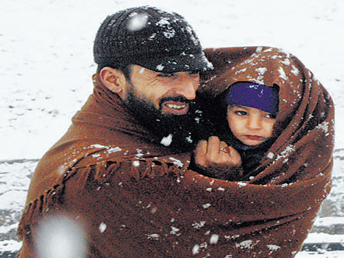 A man walks in a snow-covered garden in Srinagar 4. A man wraps his child in a shawl at Doru in Anantnag district, Jammu and Kashmir, on Monday. PTI