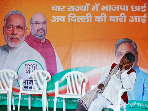 A worker of BJP takes a nap in front of the party's campaign billboard featuring PM Modi and BJP's president Shah at a party office in New Delhi. Reuters Photo