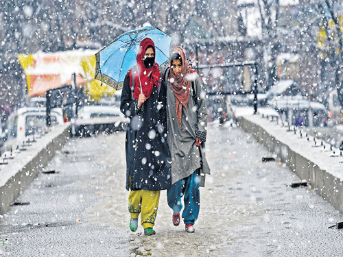 enjoying the fog: Girls walk with an umbrella during fresh snowfall on the outskirts of Srinagar on Thursday. PTI  Photo