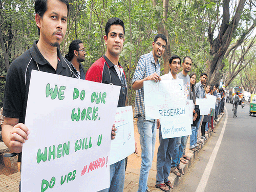 Research students form a human chain in Bengaluru on Wednesday as part of a protest to demand a hike in scholarships. DH photo
