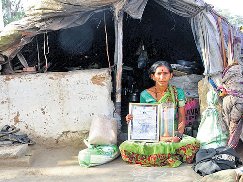 Burrakatha singer Lakshmamma poses with the Kitturu Rani Chennamma award in front of the hut that has been her home for the last 30 years. DH PHOTO