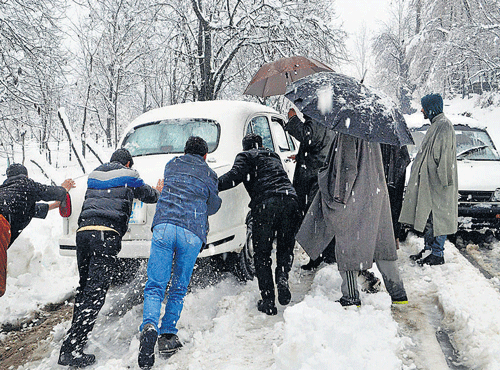 People push a vehicle stuck on a snow-covered road in the Shopian district of Jammu and Kashmir on Monday. Fresh snowfall disrupted normal life across the Kas