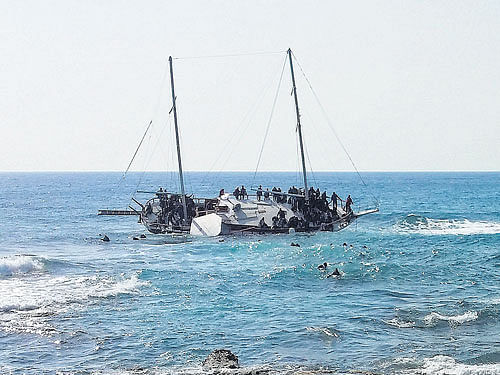 hanging on to life: Migrants are seen onboard a capsized wooden sailboat, that ran aground off the coast of the southeastern Greek island of Rhodes on Monday, as others are seen in the water trying to reach the shores. REUTERS