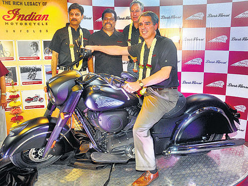 Polaris Industries Chairman and CEO Scott Wine astride on an Indian motorcycle at the company's new dealership in Bengaluru on Thursday. Company President and COO Bennett J Morgan (standing right) and Polaris India MD Pankaj Dubey (left) are also seen. DH Photo by B K Janardhan