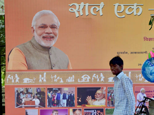 People rest near a hoarding of Prime Minister Narendra Modi highlighting the achievements of one year of NDA Government, in New Delhi on Monday. PTI Photo