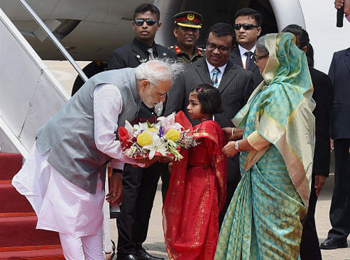 Prime Minister Narendra Modi interacts with a girl after she presented a bouquet to him upon his arrival at Hazrat Shahjalal International Airport, Kumitola in Dhaka on Saturday. Bangladeshi Prime Minister Sheikh Hasina looks on. PTI Photo
