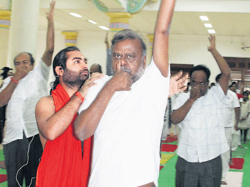 In this file picture taken on July 23, 2013, Vachanananda Swami teaches a few asanas to  Social Welfare Minister H Anjaneya during a Yoga session at the Vidhana Soudha in Bengaluru. The minister had taken part in the event held to teach Yoga to legislators.