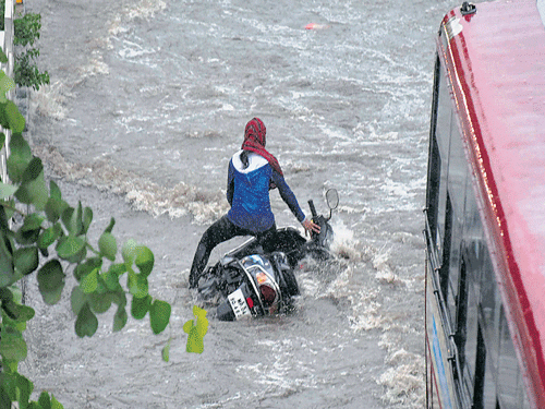A girl falls with her two-wheeler at a flooded road during first monsoon shower in Bhopal on Monday. PTI