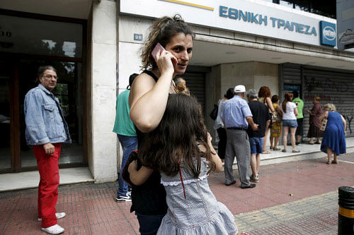 A young girl hugs her mother while lining up with other people to withdraw cash from an ATM outside a National Bank branch in Athens. Reuters