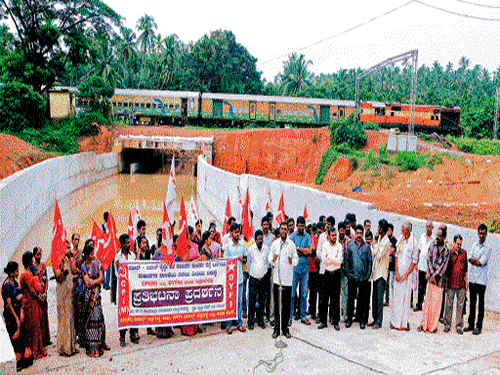 Members of CPM and DYFI stage a protest demanding approach road to RUB, on Padil-Bajal road on Monday. dh photo
