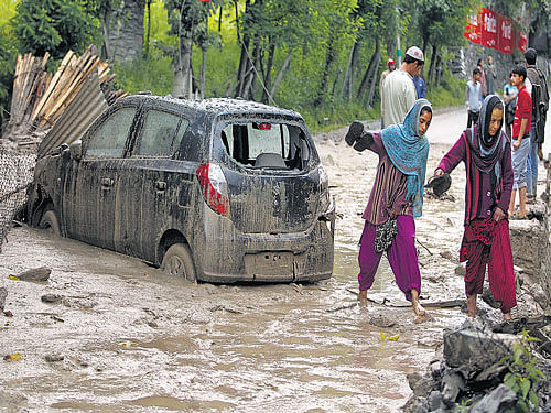 caught in mud: Villagers walk next to a damaged car in the cloudburst-hit area of Kullan village in Ganderbal district of Jammu and Kashmir, on Friday. reuters