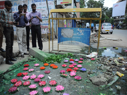 Artist Baadal Nanjundaswamy creates an art work by installing artificial lotus flowers over a sewage leackage on footpath, dh photo
