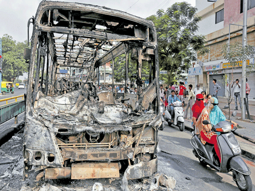 Commuters ride motocycles next to the wreckage of a bus that was burnt in the clashes between the  police and protesters in Ahmedabad on Wednesday. Reuters