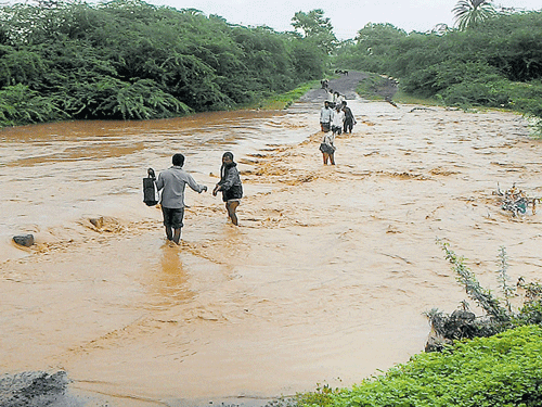 Local residents wade through water overflowing on a bridge at Aralichandi village near Basavana Bagewadi in Vijayapura district on Wednesday. DH PHOTO