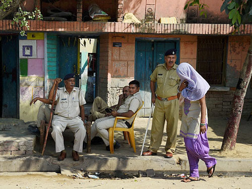 A woman walks past police men deployed in the Sunpedh village where a dalit's house was set on fire allegedly by men belonging to the upper-caste, at Sunpedh village in Ballabhgarh, Faridabad on Friday. PTI Photo