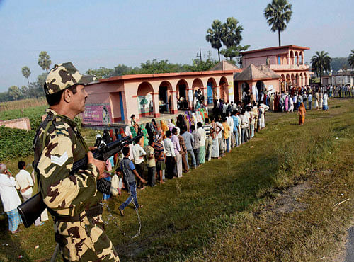 A security person guards as voters wait in queues to cast their votes during fourth phase of Bihar elections in Muzaffarpur on Sunday. PTI Photo