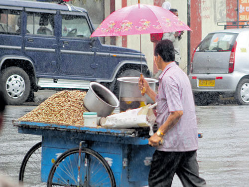 A street vendor walks with an umbrella after showers lashed the City on Sunday. DH photo
