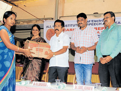 Jyothi from Sairanga Vidya Samsthe hands over 50 hearing aids, brought for repair, to MLA M K Somashekhar at the inauguration of a repair camp at All India Institute of Speech and Hearing (AIISH), in Mysuru, on Monday. DH photo