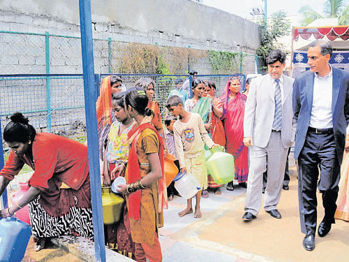 US Ambassador to India Richard R Verma (extreme right) at a potable water collection point in a slum in Lingarajapuram  on Tuesday. Waterhealth India Private Limited chief operating officer Vishal Shah is seen. DH photo