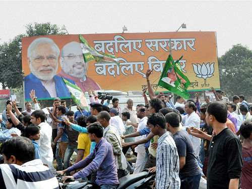 JD(U) supporters walk past a hoarding of BJP as they celebrate the Mahagathbandhan's victory in Bihar assembly elections in Patna on Sunday. PTI Photo